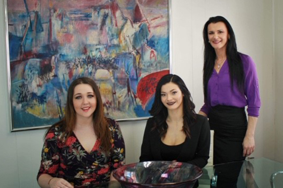About Our Agency - Arica, Emily and Shyenne Sitting and Standing Together Near an Abstract Painting