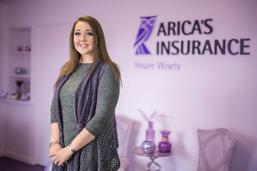Client Center - Emily Standing in Arica's Insurance Office With a Display of the Owl Logo on the Wall