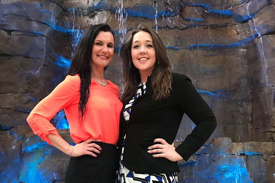 Employee Benefits - Arica and Emily Standing in Front of a Stone Waterfall With a Blue Lighting Display